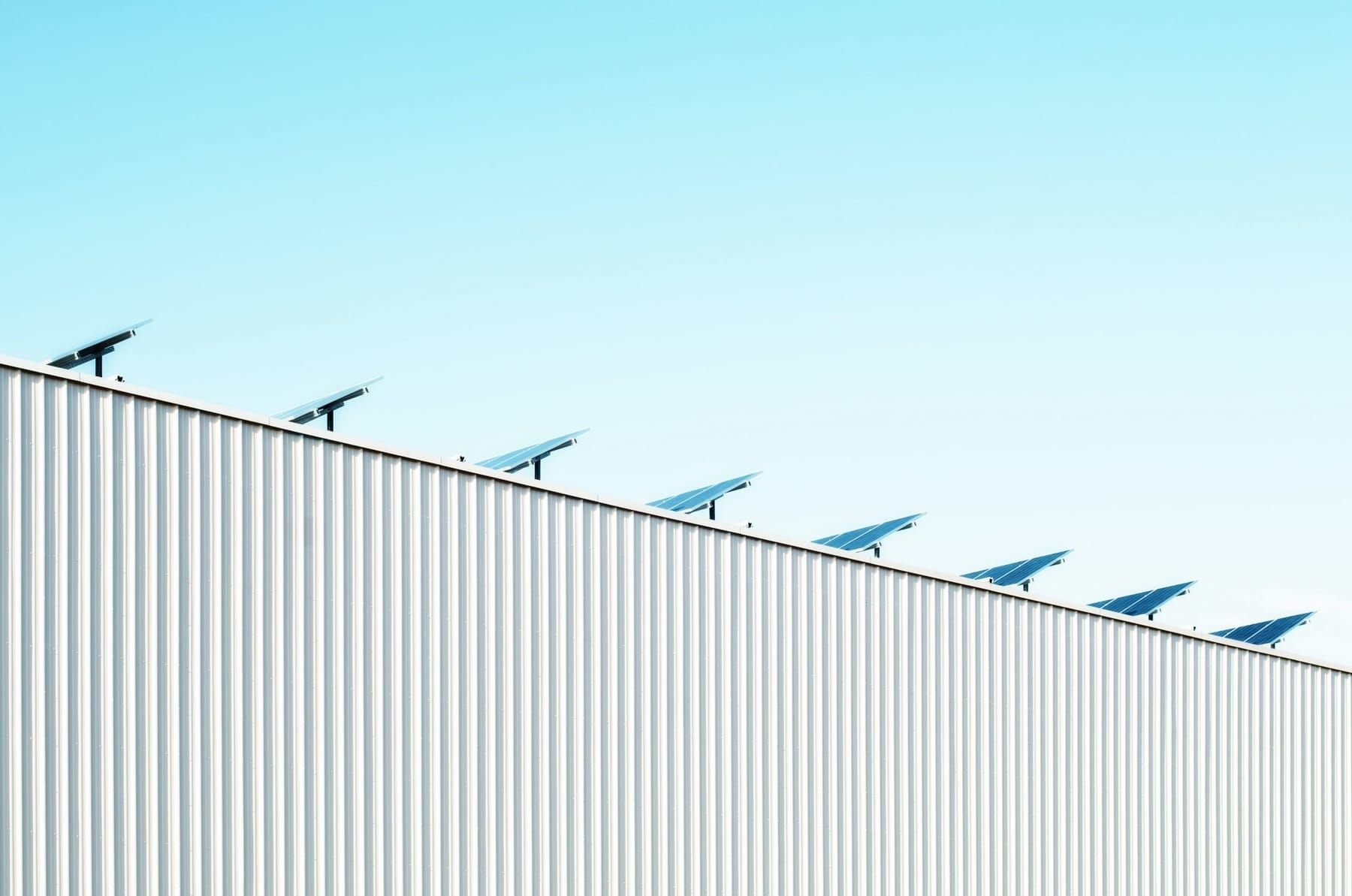 Zonnepanelen boven de rand van een bedrijfsdak tegen een blauwe lucht